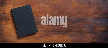 Blank cover book on a table. Closed old black hardcover notebook on wooden background, top view, banner. Copy space, template Stock Photo
