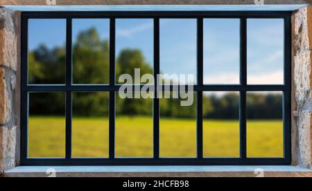 Metal frame window on a stone wall. Black color aluminum grid, blur nature background outdoors. House in countryside, window with view Stock Photo