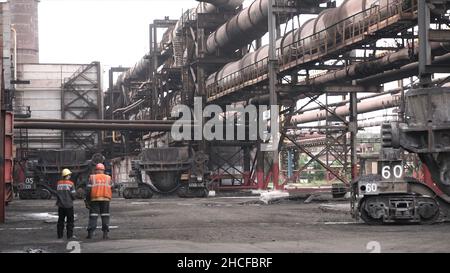 Metal melting vats being transported on big carts to the metal melting shop, heavy industry concept. Two male workers in uniform standing outdoors at Stock Photo