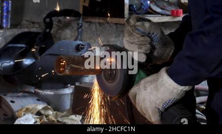 Male hand cuts off pieces of water pipe with angle grinder. Cutting of a steel with splashes of sparks at construction site. Sparks during cutting of Stock Photo