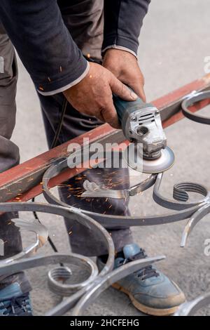Man grinds metal with angle grinder in metal workshop. Sparks fly on the sides. Male hand and instrument. Vertical frame, close-up. Stock Photo