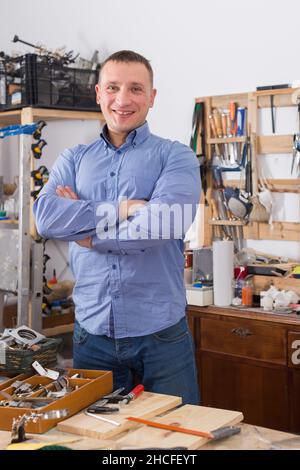 Portrait of happy young handsome carpenter in workshop. Stock Photo
