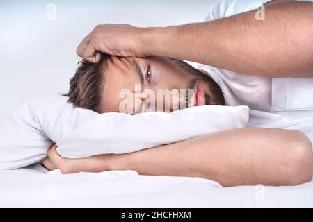 Man with depressive disorder lying on the pillow in the bed. Depressed man with negative thoughts. Stock Photo