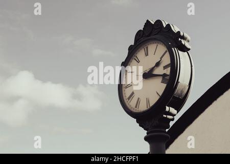 Street clock with cloudy gray sky background. Stock Photo
