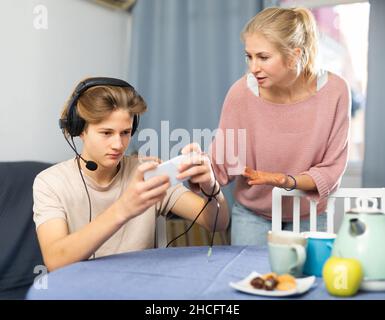 Teenage son listening music in headphones or playing online games ignoring  his mother Stock Photo - Alamy