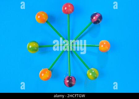 Colorful lollipops on green sticks in round. Multicolored candies on blue background, top view. Summer and pop art concept. Flat lay. Real reflection Stock Photo