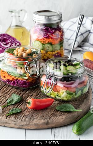 Three fresh homemade salad jars on a wooden board, ready for eating. Stock Photo