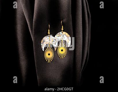 Metal earrings hanging on black silk background. Stock Photo