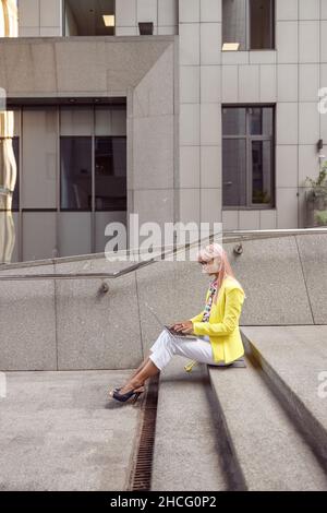 Female smiling while typing on laptop on street stairs Stock Photo