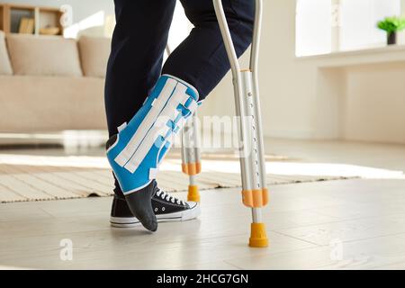 Leg of man walking with crutches in ankle brace with support adjustable strap fracture fixator. Stock Photo