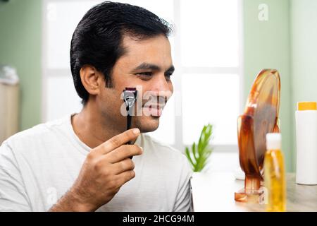 Handsome young Man using derma roller on face by looking at mirror - concept of treatment or therapy for skin, acne scarring and dermatology. Stock Photo