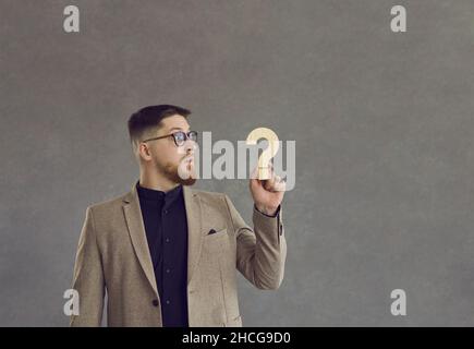 Confused and surprised businessman looking at question mark he is holding in his hand Stock Photo