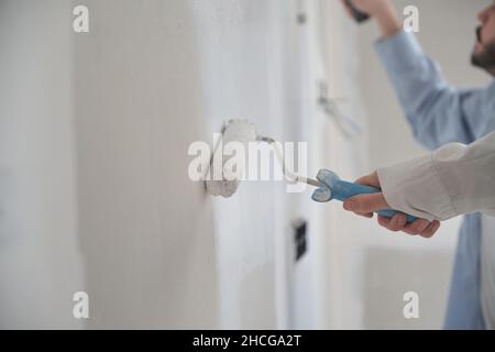 Unrecognizable young couple painting walls in their new house in construction. Stock Photo