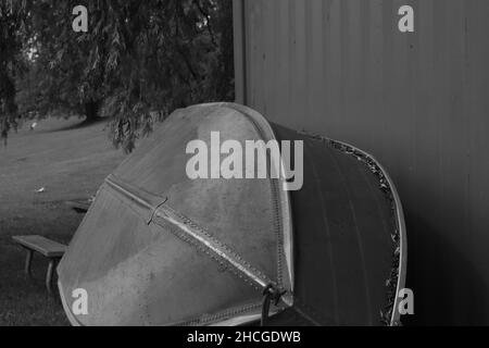 Grayscale shot of an old boat near the house on the lakeshore Stock Photo