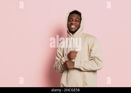 Smiling guy, young dark skinned man wearing hoodie, youth clothes isolated on pink studio background with copyspace for ad. Stock Photo