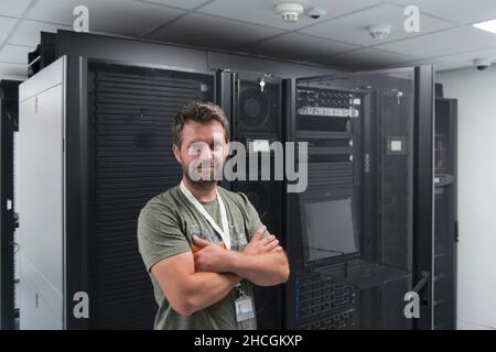 Portrait of male technician or network administrator standing brave as a hero with arms crossed in data center server room. Stock Photo