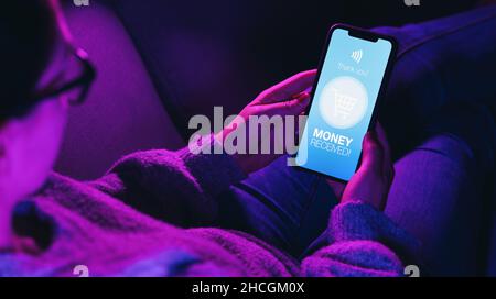 Woman lies on sofa and Received Payment or Money message on a mobile phone screen.  mobile phone with imaginary Banking or Payment service. Online bil Stock Photo