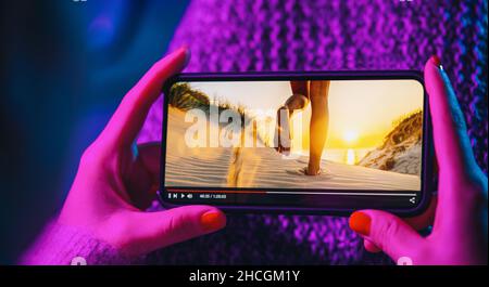 Online movie stream with smartphone. Woman watching film on mobile phone with imaginary video player service. Stock Photo