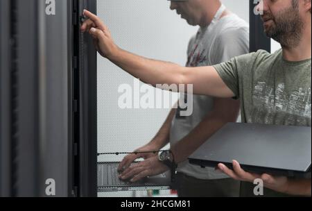 Technicians team updating hardware inspecting system performance in super computer server room or cryptocurrency mining farm. Stock Photo