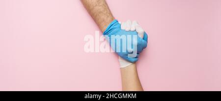 Doctor's hands or helpers hands in gloves holding together hands. Fight together in the Corona pandemic. Medical banner with copy space on pink backgr Stock Photo