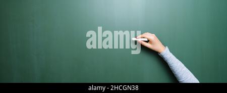 Blank blackboard / chalkboard, hand writing on green chalk board holding chalk, with copyspace for your individual text. Stock Photo