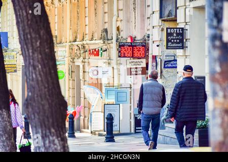 People walking down the street in rustaveli avenue with exchange office electric board and daily exchange rates displayed.Concept of economics crisis Stock Photo