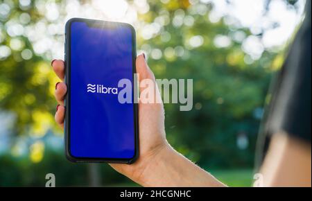 Woman hand holding iphone Xs with logo of Libra in the park. Libra Facebook cryptocurrency and bitcoin cryptocurrency smartphone share, Libra coins Stock Photo