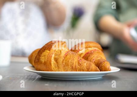 delicious croissants lie on a plate on the kitchen table. in the background the silhouettes of two women in blur. the concept of women's conversation Stock Photo