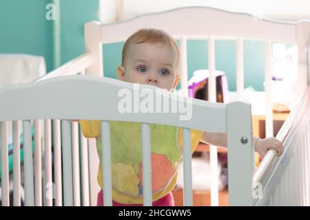 A small child looks out of the crib. Stock Photo