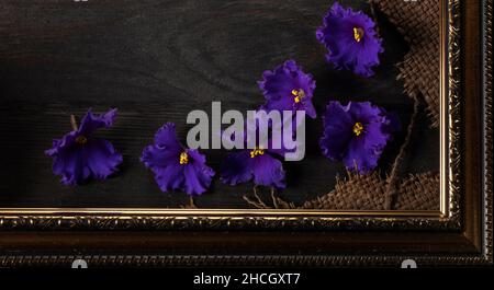 Part of a beautiful frame contains rough weave fabric on a wooden background and violet flowers. Background for the inscription. Stock Photo