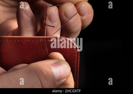 Making leather wallets. The hands of the master sew a leather product. Stock Photo