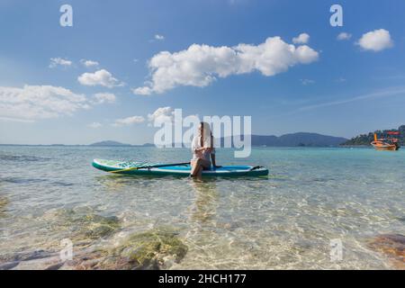 Woman wearing sunglasses sitting on the paddleboard on a water. Stock Photo