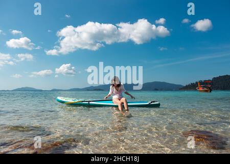 Woman wearing sunglasses sitting on the paddleboard on water. Stock Photo