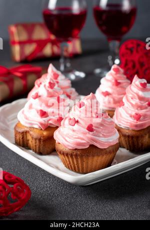 Homemade cupcakes decorated with cream and heart-shaped sprinkles for Valentine's Day on gray background, Vertical format Stock Photo
