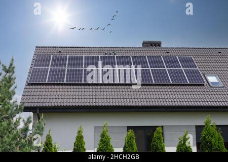 Solar panels on houseroof in front of blue sky with sun. Solar Panels On House Roof. Sustainable Renewable Energy. Stock Photo