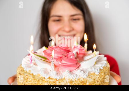 A brunette woman in red clothes holds a large white cake with candles, makes a wish Stock Photo