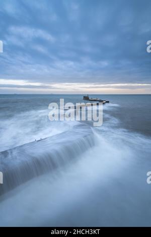 Waves crashing over the iconic zig-zag breakwater at St Monans harbour in the East Neuk of Fife, Scotland, UK.