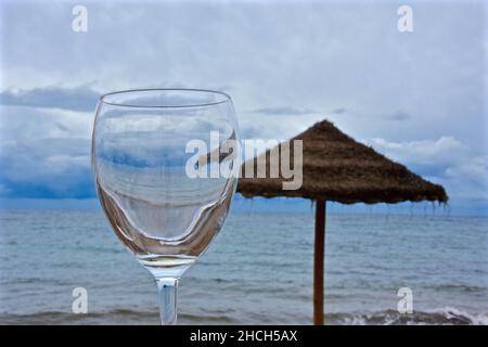 Empty wine glass in front of a sisal parasol by the sea Stock Photo