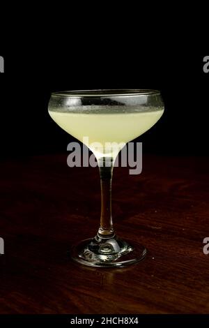 Vertical shot of a glass of Corpse Reviver cocktail on the table with a dark blurry background Stock Photo