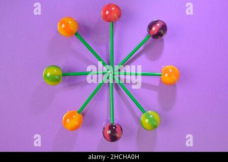 Colorful lollipops on green sticks in round. Multicolored candies on mauve background, top view. Summer and pop art concept. Flat lay. Real reflection Stock Photo