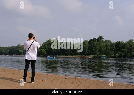 young man with back to camera photographing pleasure boats on the Hyde Park Serpentine London UK. Stock Photo
