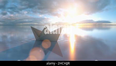 Paper boat in a calm sea at sunrise sunset with cloudy sky Stock Photo