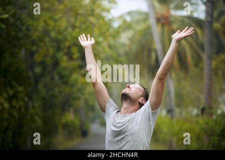Portrait of drenched man with eyes closed enjoying heavy rain in nature. Stock Photo