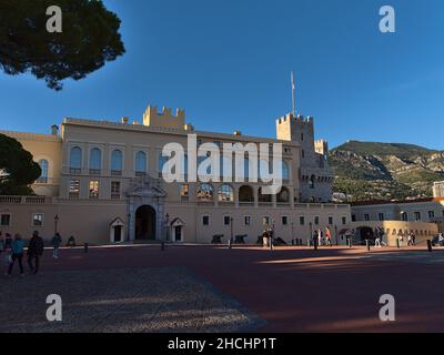 View of famous Prince's Palace of Monaco, the official residence of the Sovereign Prince, in the afternoon with tourists walking by and mountains. Stock Photo