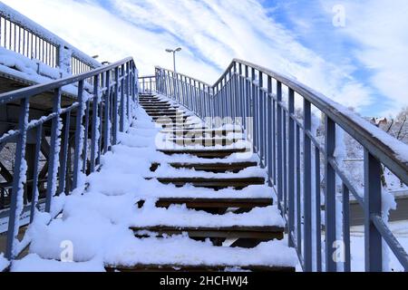 A staircase with a metal railing, covered with snow in winter, leads to the bridge. Element of architecture, design on a city street. Dnipro city Stock Photo