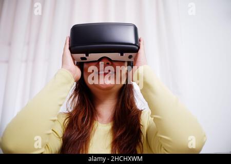 Young asian woman wearing virtual reality glasses at home. VR headset. VR concept. Stock Photo