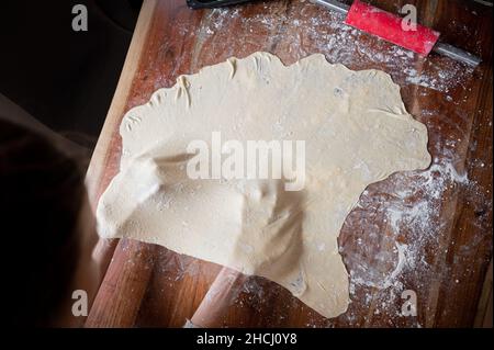 Top view of female hands pulling and stretching home made vegan pastry dough for a strudel or sour pie on a flour dusted table. Stock Photo