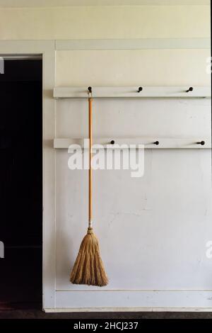 A read broom hangs from a peg on the wall -- two classic Shaker inventions. Canterbury Shaker Village, New Hampshire USA. Stock Photo