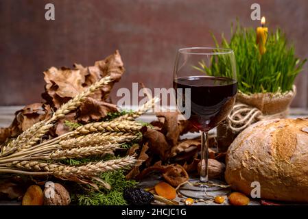 Traditional food for orthodox Christmas eve. Yule log or badnjak, wine, bread, cereals, dried fruits and burning candle on rustic table. Concept celeb Stock Photo