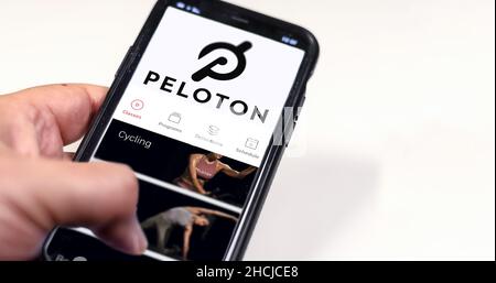 New York, USA, July 2021: A hand holding a phone with the Peloton app on the screen isolated on a white background. Peloton is an American exercise eq Stock Photo
